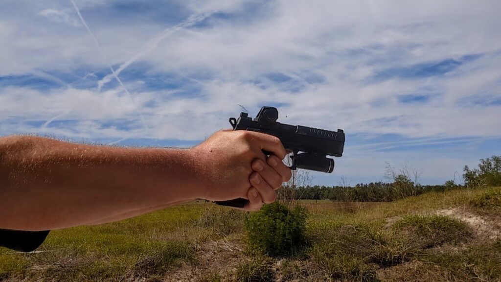 Profile view of a person aiming a CZ P-09 F Nocturne pistol equipped with a Steiner MPS-C red dot and a weapon light against a bright sky.