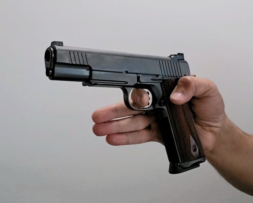 A 1911 pistol being held with only the thumb and trigger finger.