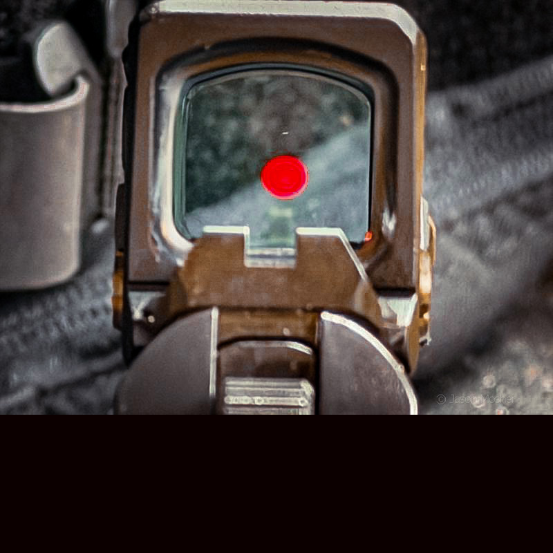 A view looking through the COA optic, showing the red dot and the iron sights of the Operator pistol. 