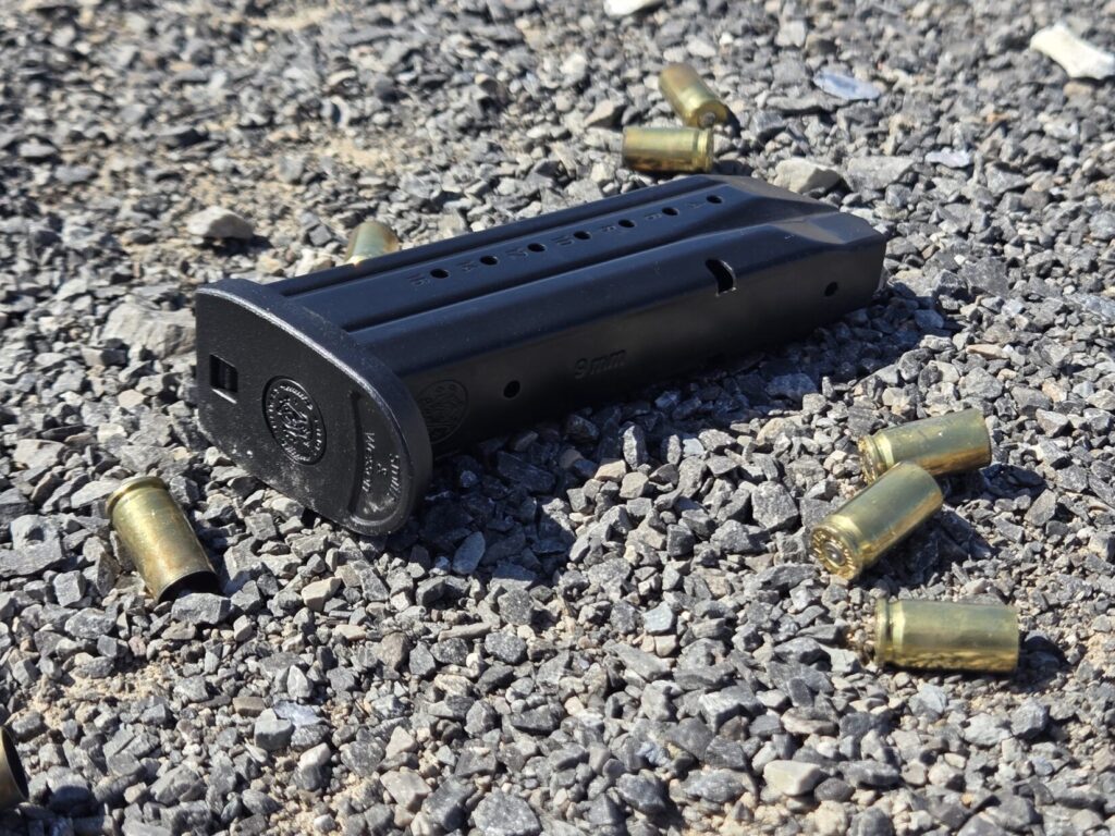 An empty M&P pistol magazine on a gravel backdrop with empty 9mm casings
