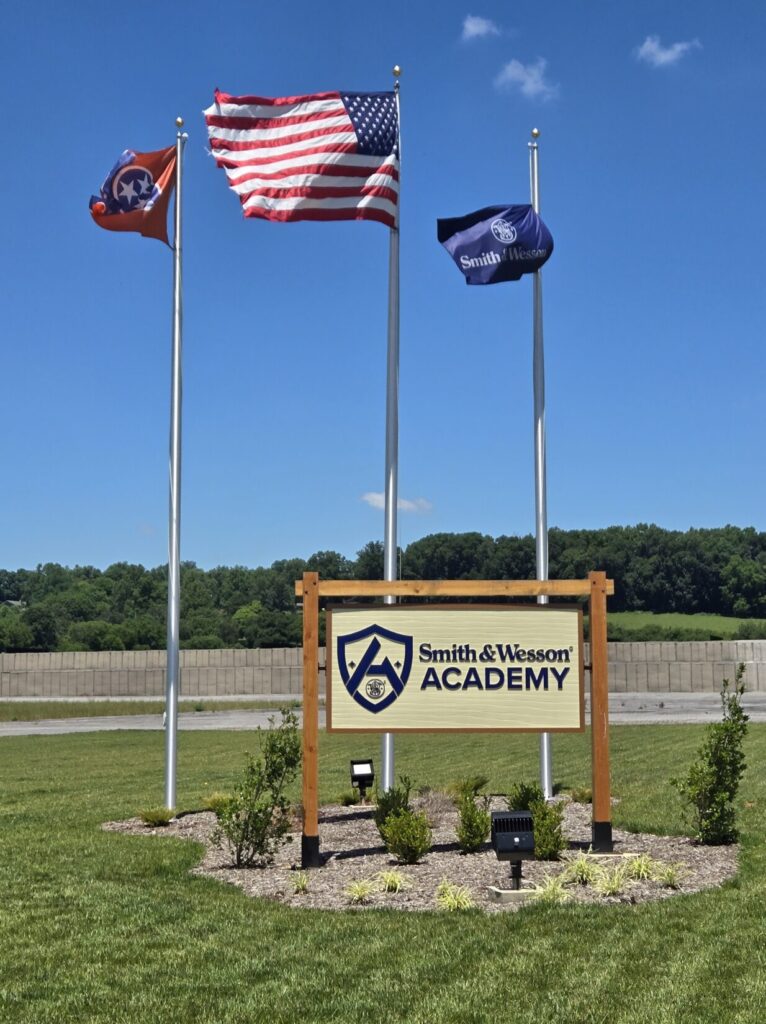 A sign for Smith & Wesson Academy with multiple flags in the background