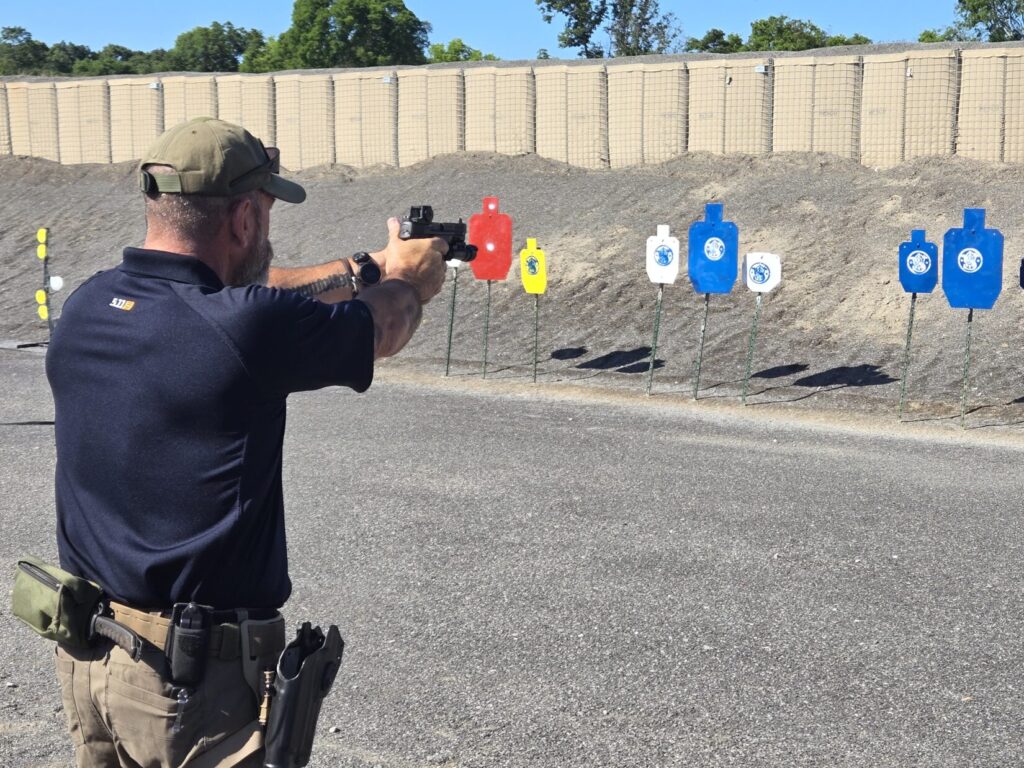 A man aims at a steel target on a range with steel targets in the backdrop