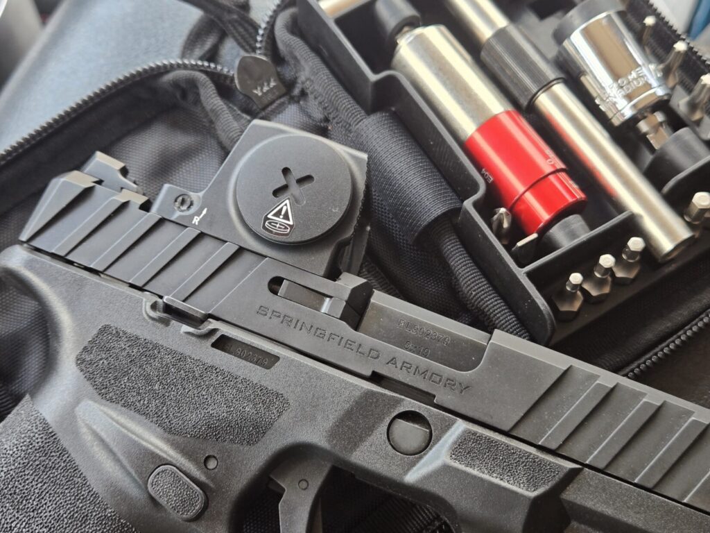 A pistol red dot on top of a pistol with tools in the background