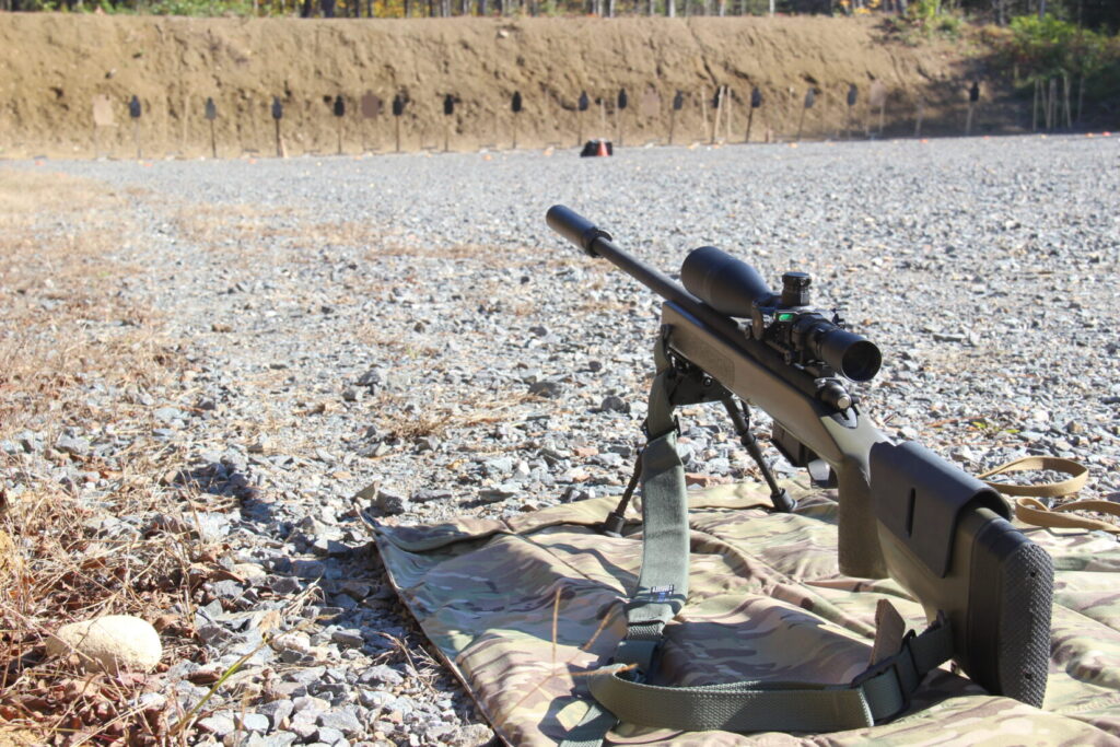 A precision bolt-action rifle with suppressor pointed downrange at steel