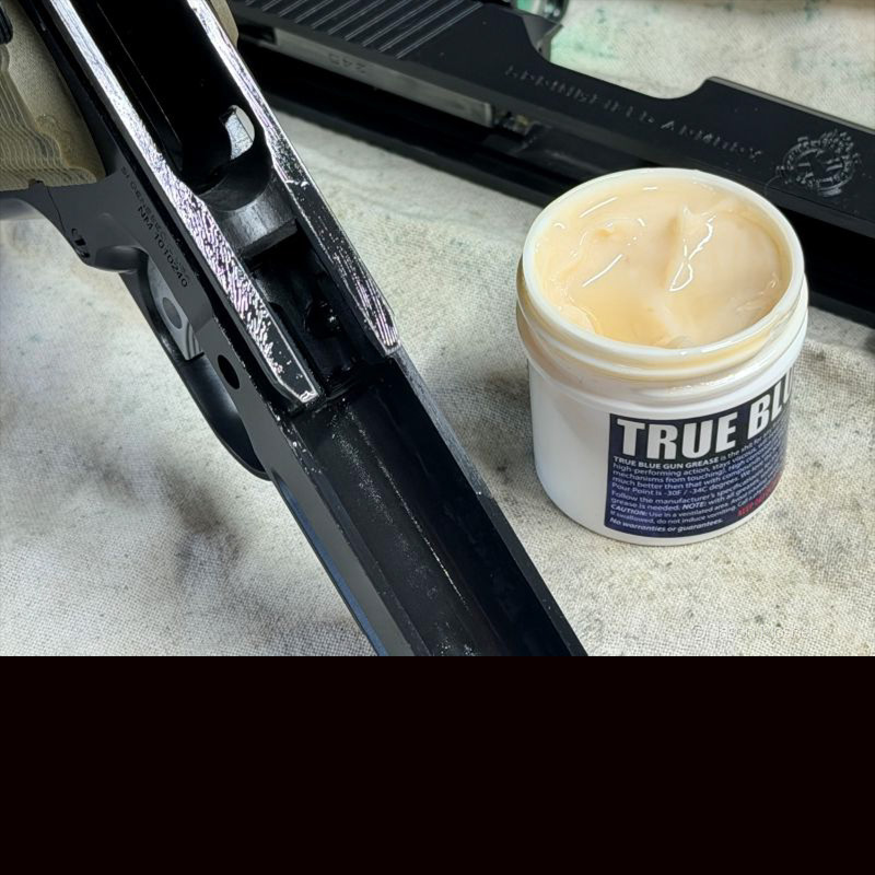 A bottle of grease sitting next to the frame of a 1911 handgun on a white cloth.