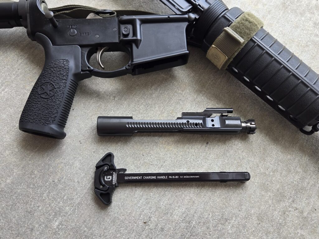 A charging handle and bolt carrier group next to a broken down AR