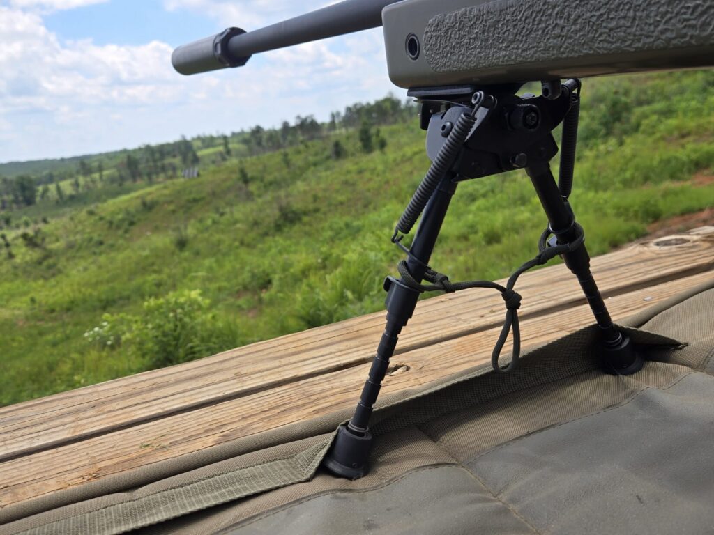 A rifle bipod on a shooting mat with the rifle aimed downrange