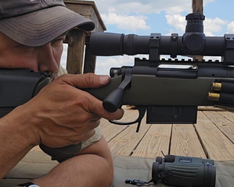 A man behind a precision rifle looking downrange on a wooden platform