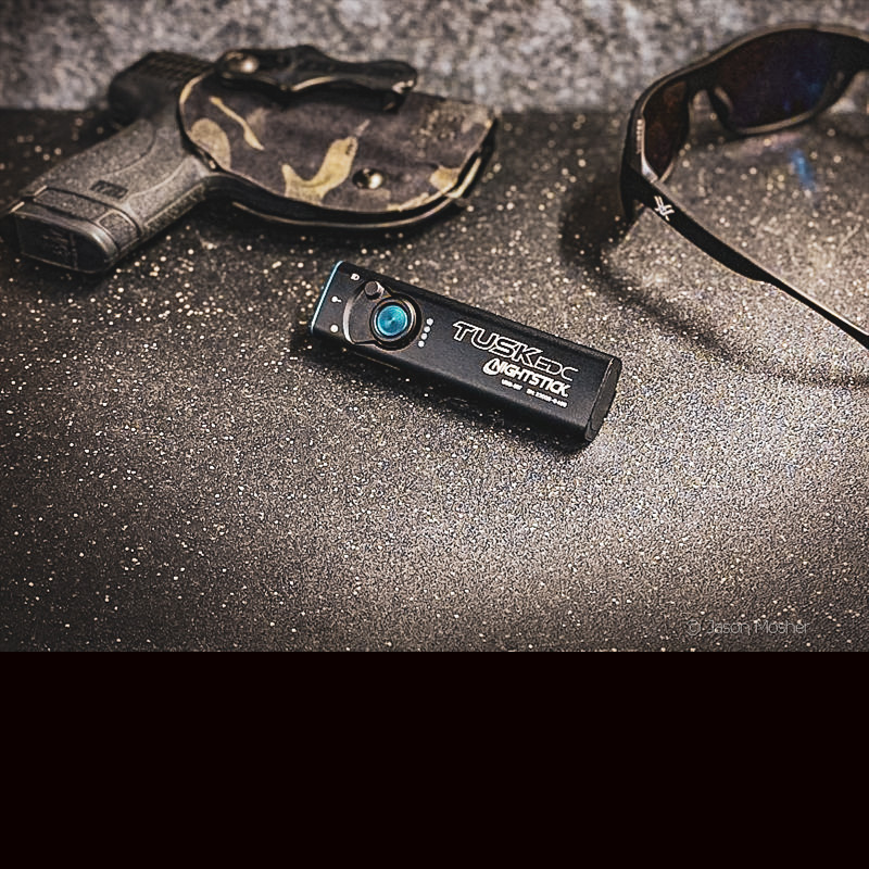 A black light laying next to a handgun and sun glasses on a black table.