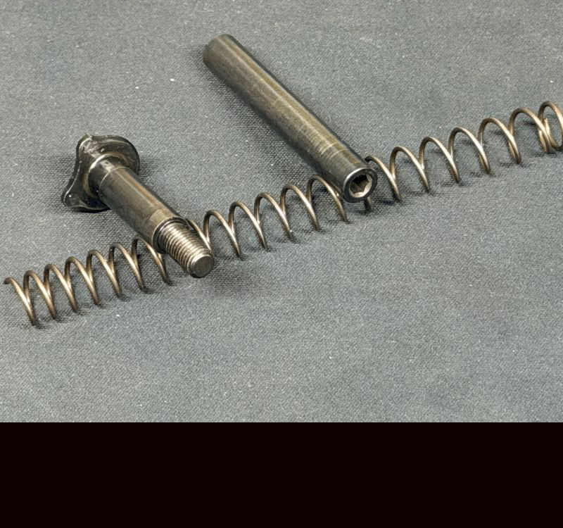 A spring and both pieces of a metal guide rod laying on a grey counter. 