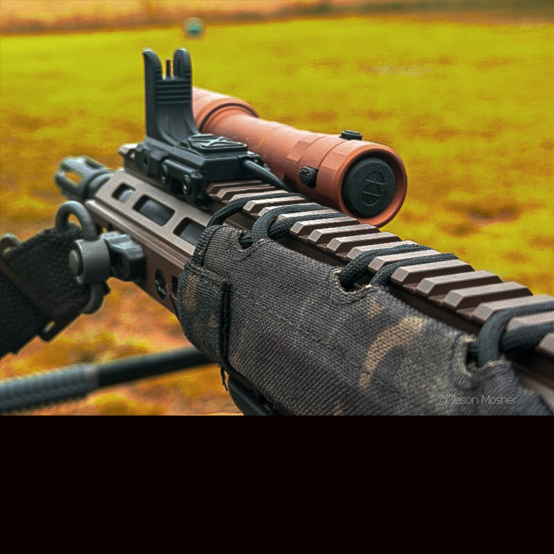A view from the back of the RIEN light mounted to a rifle, with a green field in the background. 