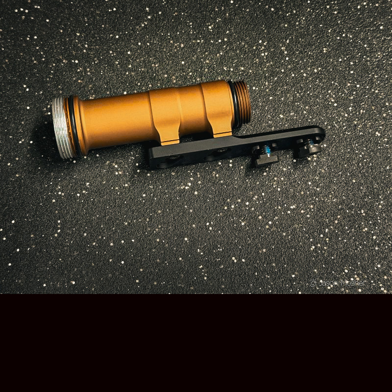 The middle part of the REIN light with a black bracket attached to it, laying on a black surface. 