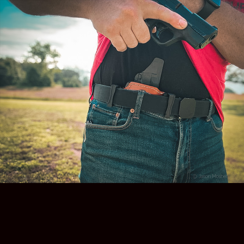 A person in jeans and a red shirt, drawing a gun from the Shenandoah holster.