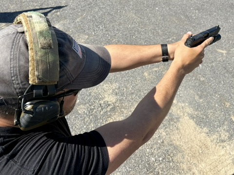 A shooter with a pistol, hat, eye protection, and hearing protection
