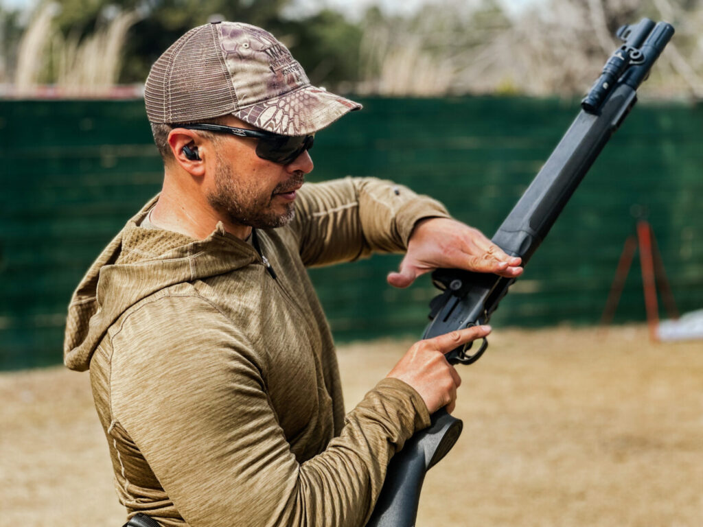 A man in a fleece top and kryptek ball cap with a shotgun