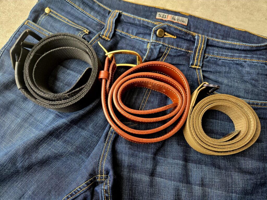 A pair of jeans with three belts on top of the front pockets.