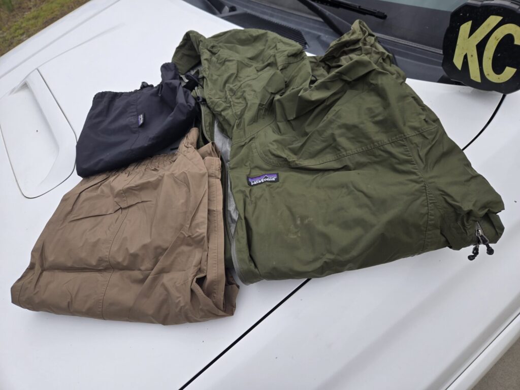 A rain jacket, a set of rain pants, and a stuff sack on top of a vehicle hood.