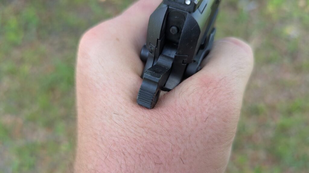 An extreme close-up view from behind the hammer and slide of a black handgun being held in a person's hand, highlighting the rear sight and texturing on the hammer.