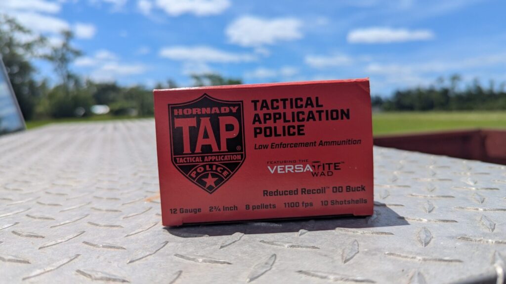A red box of Hornady TAP Tactical Application Police shotgun ammunition sitting upright on a silver diamond-plate surface with a blurry outdoor background.