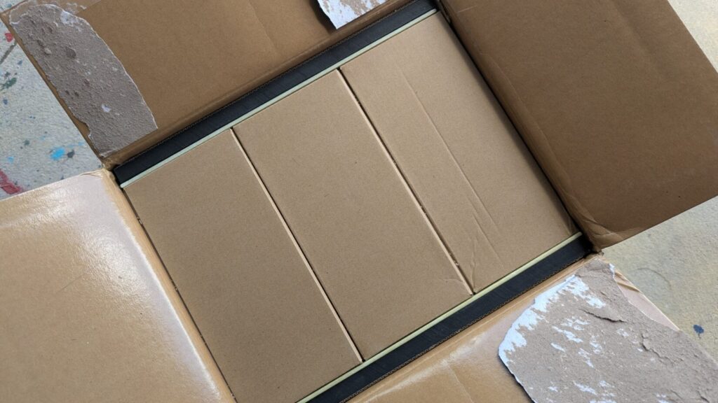 Looking down into an open cardboard shipping box containing three smaller, rectangular cardboard boxes packed tightly side-by-side.