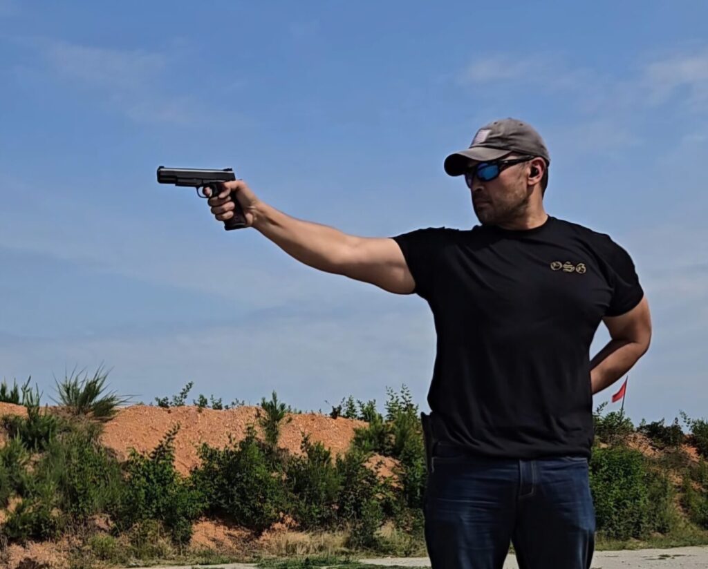 A man in a black shirt holds a 1911 with an extended arm at a range