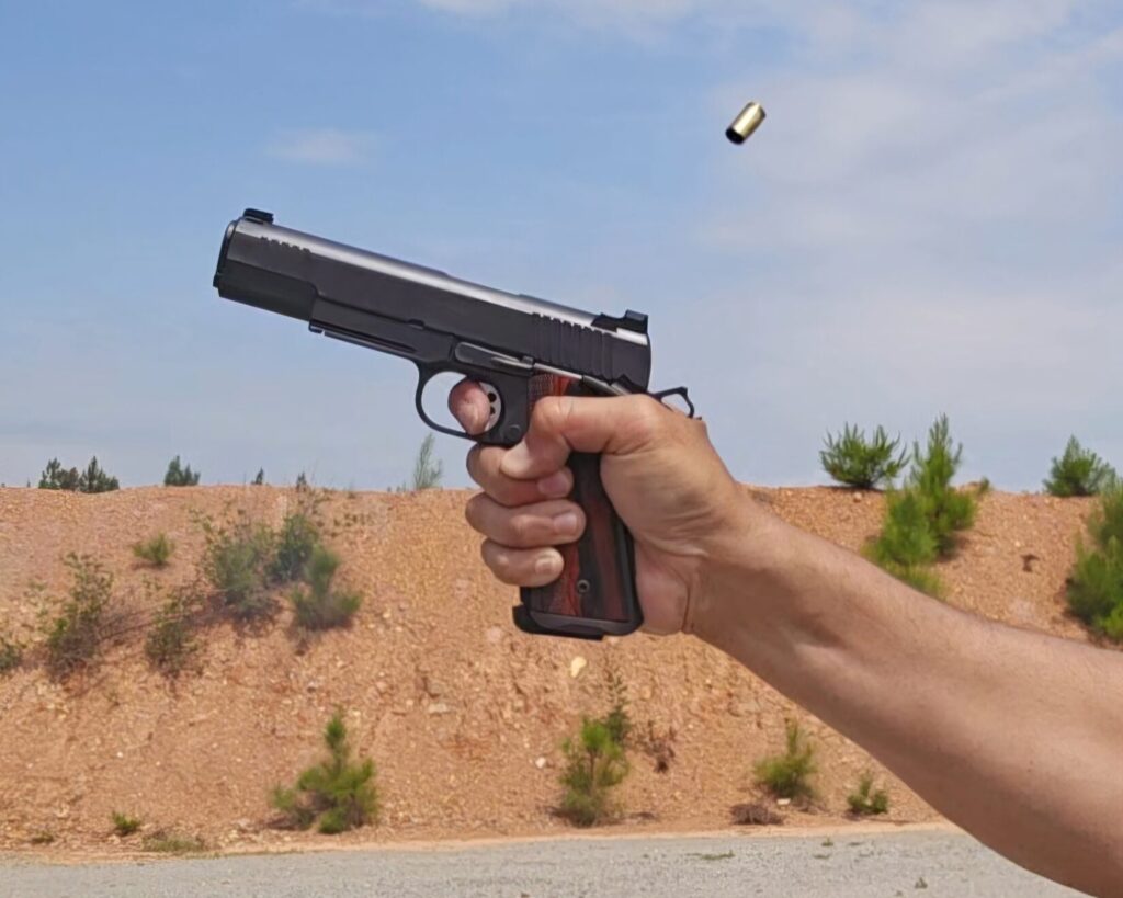 A pistol mid recoil with brass in the air at a shooting range