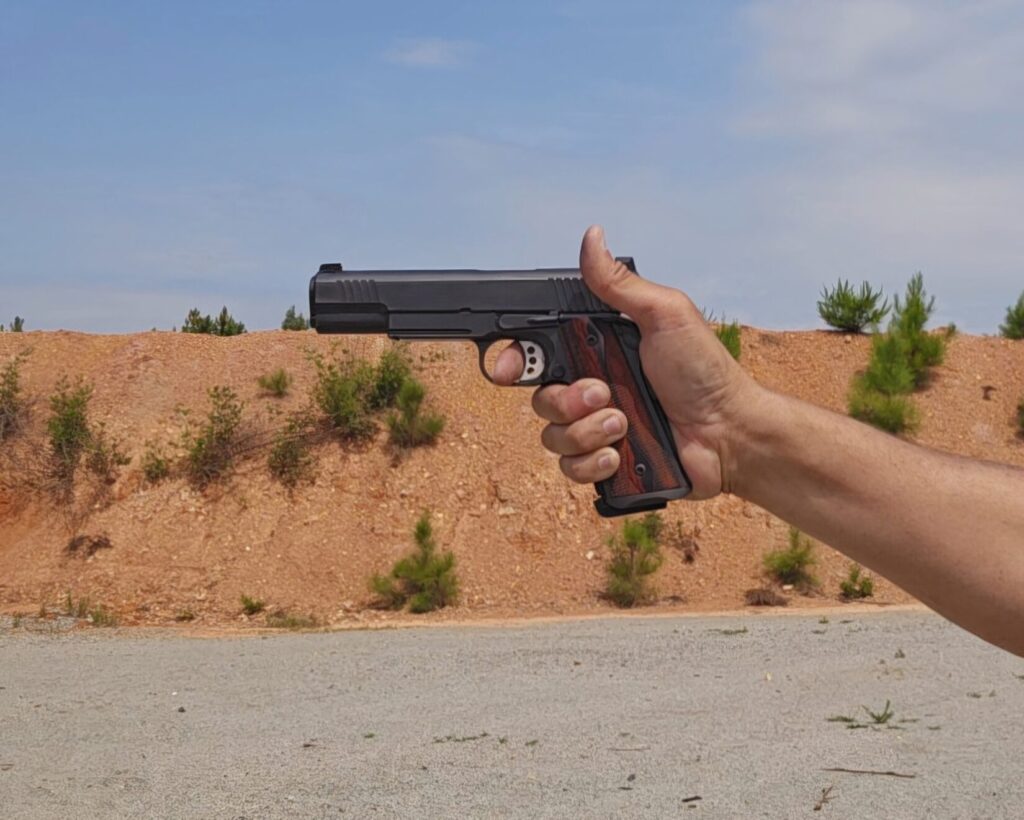 A 1911 pistol aimed with one hand at a shooting range