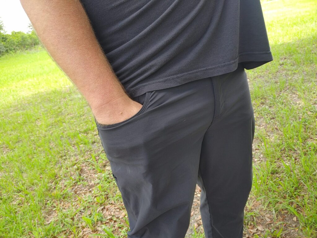 High-angle close-up of a man's right hand reaching into his front pants pocket to grip a concealed pocket pistol.