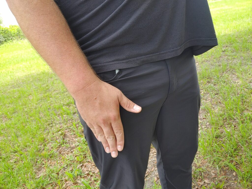 Close-up side view of a man pressing his right hand flat against his front pants pocket, revealing the distinct outline (printing) of a concealed handgun.