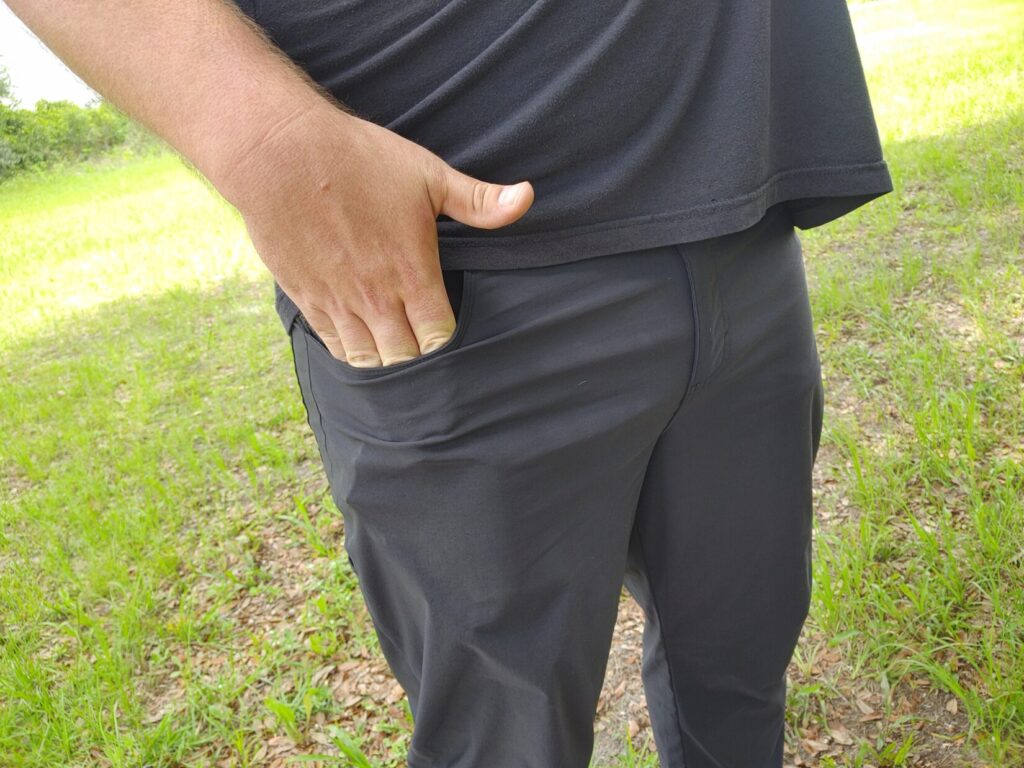 Close-up side view of a man resting his right hand naturally against his thigh just below the front pocket line, with a slight protrusion from a concealed firearm visible.