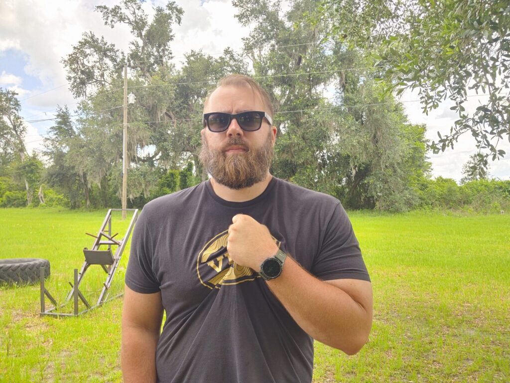 Front view of a bearded man with his left hand grabbing the center of his t-shirt to begin a pocket carry draw sequence.
