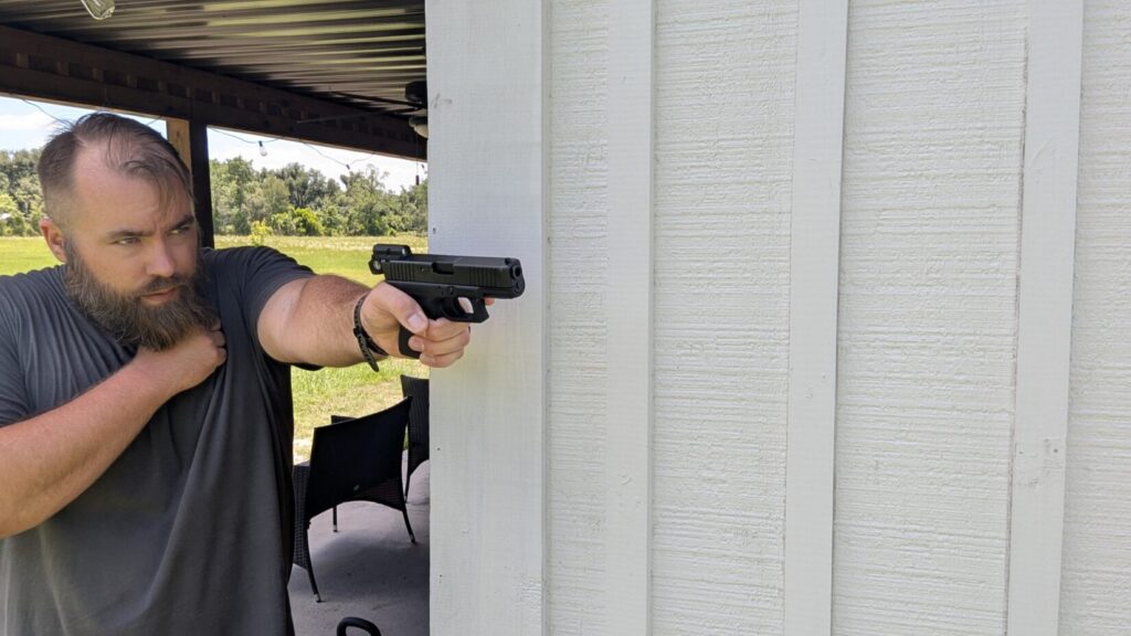 A man aiming a handgun with a minimalist tube-style red dot sight that has an exceptionally small, narrow lens profile.