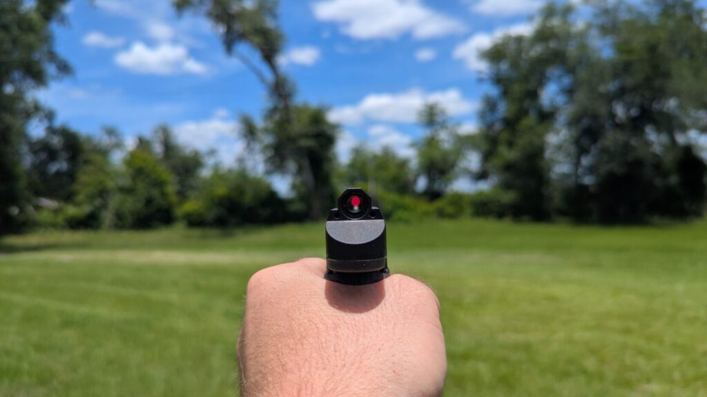 Point-of-view look through an enclosed ultra-compact tube sight, showing a very small circular lens filled almost entirely by a bright red dot.