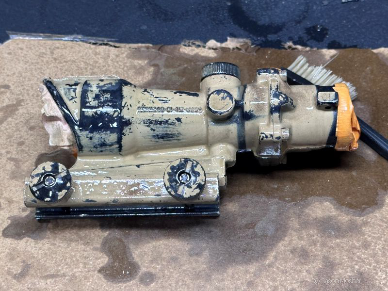 A black ACOG optic with brown paint all over it, during the process of removing the paint.
