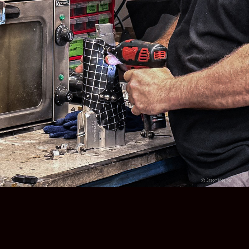 A person in a black shirt, putting a black holster over a silver holster mold.