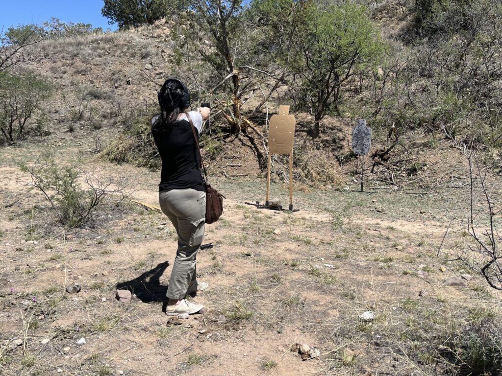 A woman who just stepped right to get a clear line-of-fire engages a steel target behind a cardboard target.