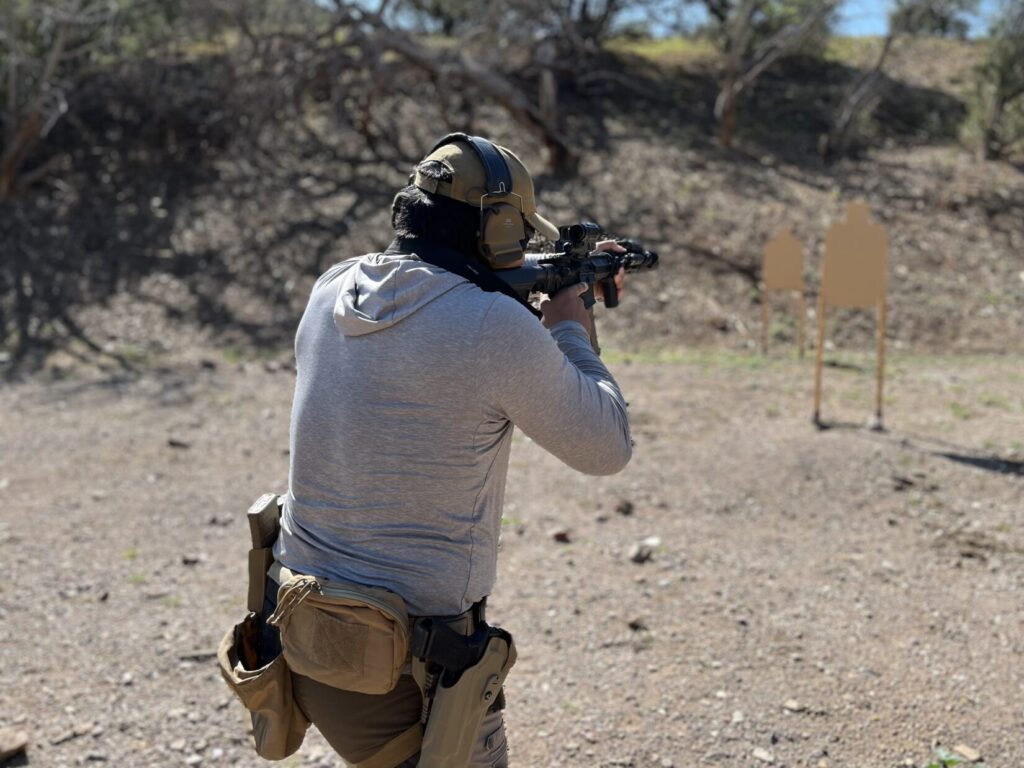 A man with an AR-series rifle aims at one of two cardboard targets after stepping left to get clear line-of-fire.