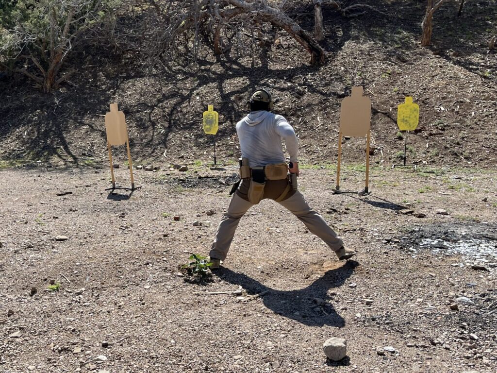 A man side-steps aggressively to get a clear line of fire. In front of him is a two-deep cue of targets.