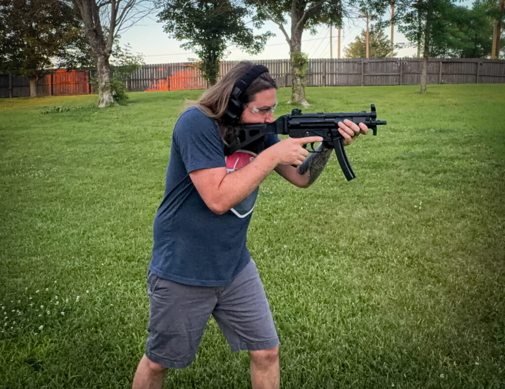 man shooting an MP5-style pistol in a field