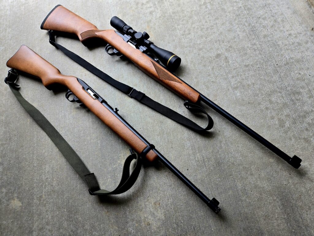 Two Ruger 10/22 Rifles with slings against a concrete backdrop