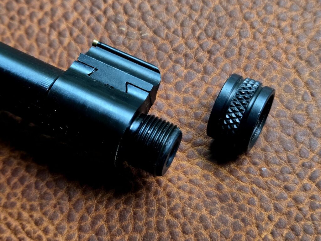 A threaded barrel and thread protector against a leather backdrop