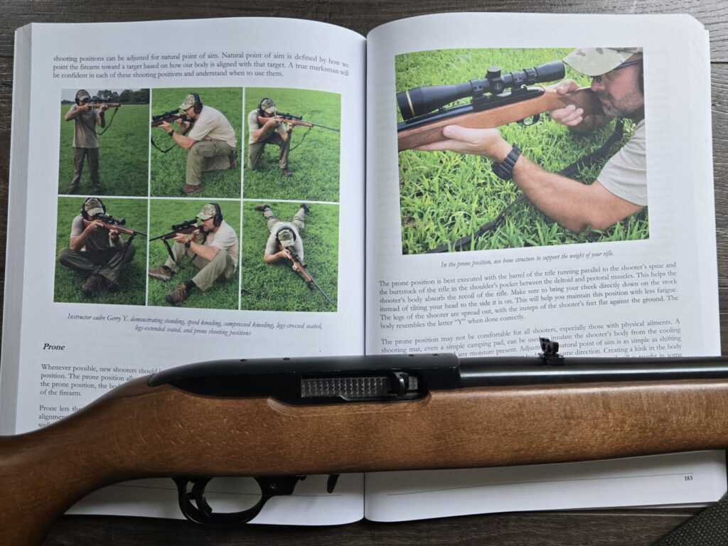 A book opened to a chapter on marksmanship with a rifle across it.