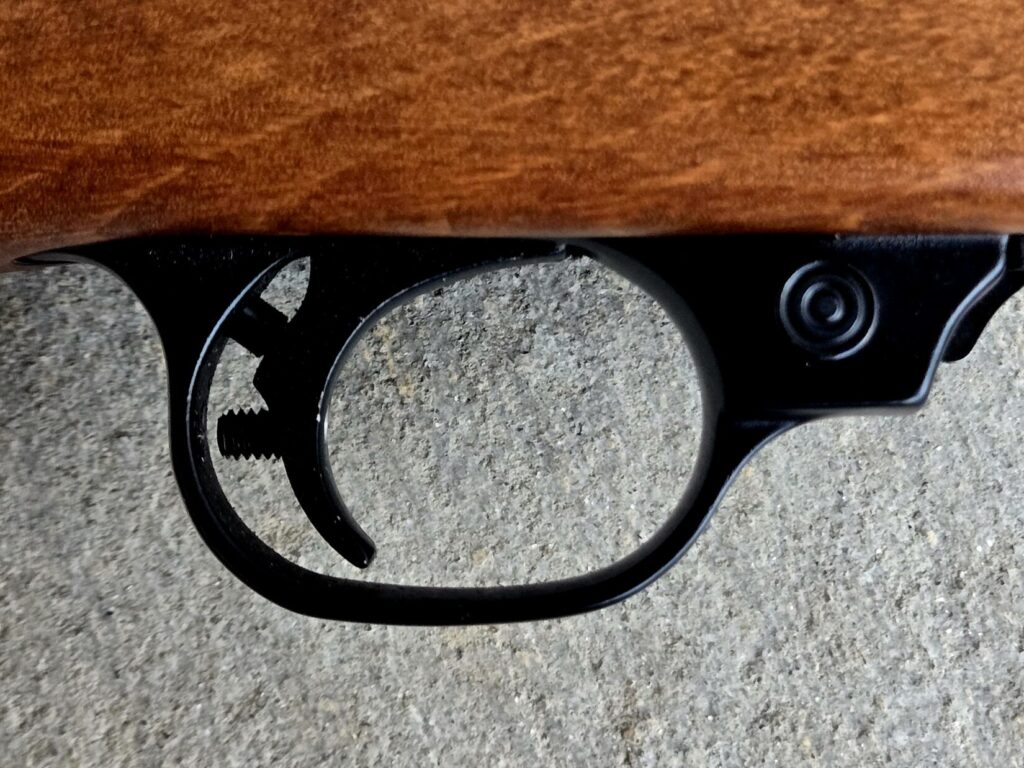 A close up photo of a trigger group on a rifle with a wooden stock