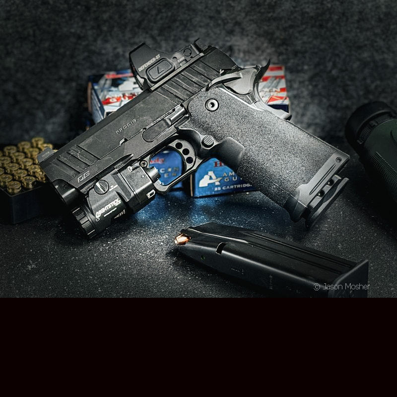 A black 1911 leaning up against some boxes of ammo, against a black background.