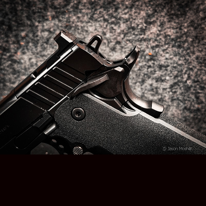 A view of the side of the hammer on a black 1911 handgun with a grey background.