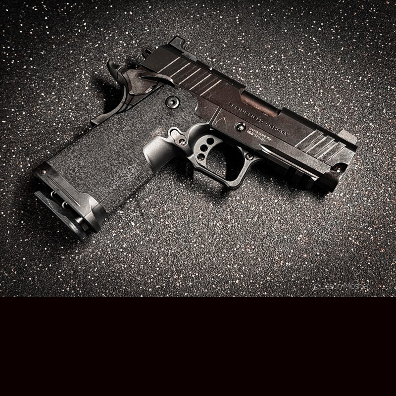 A black 1911 handgun on a grey surface.
