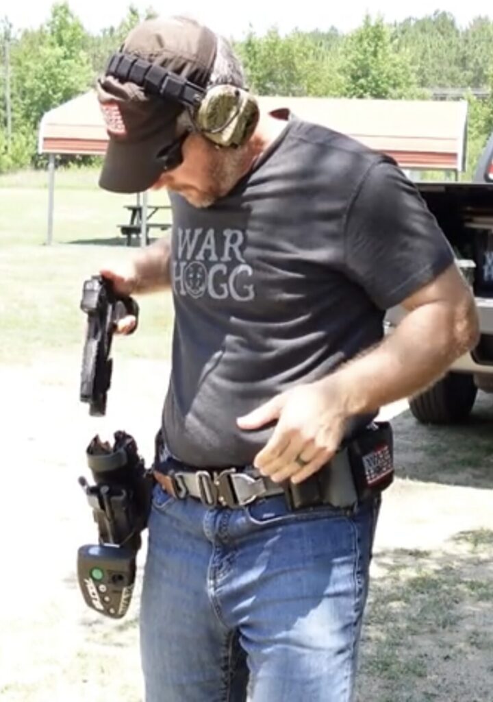 Pictured is Rick Hogg of War HOGG Tactical looking at his holster as he is reholstering his pistol.