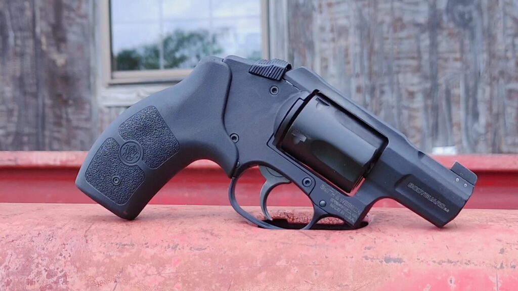 A side profile of the black Bodyguard 2.0 compact revolver resting upright on a weathered red metal surface.