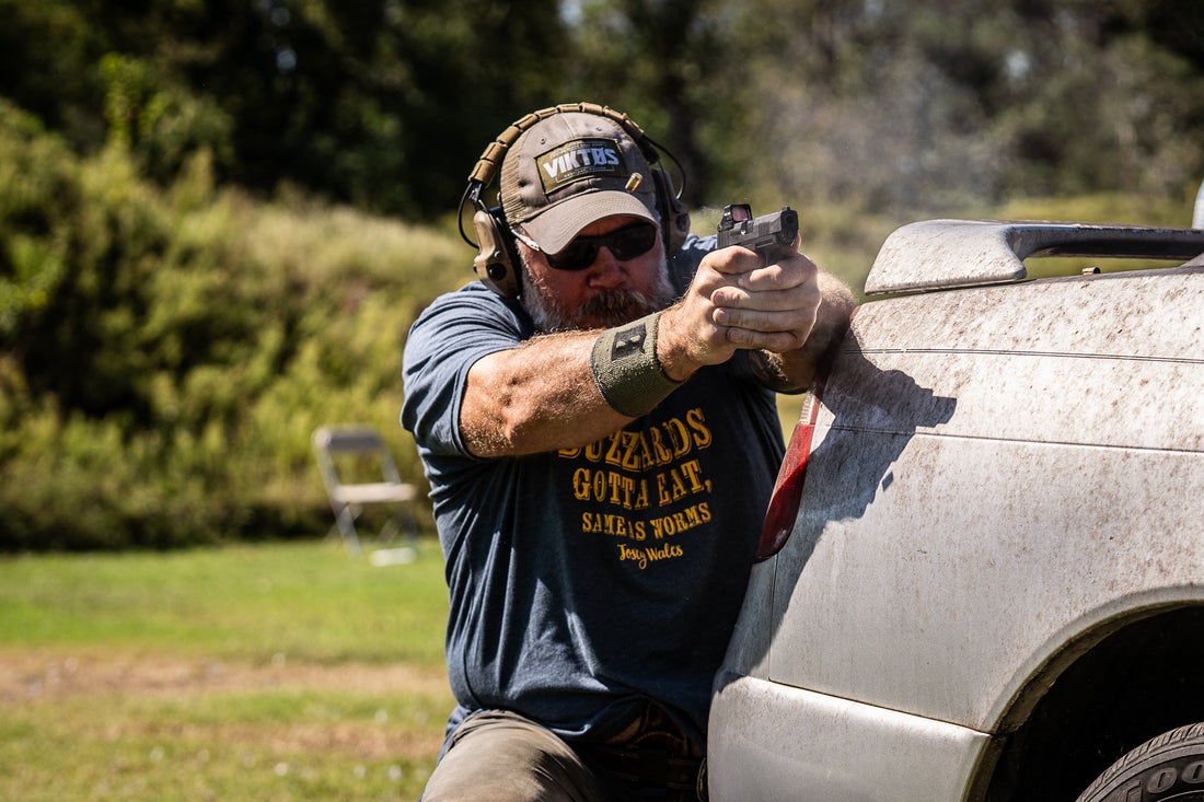 Dan brokos wearing Liberator hearing protection, kneeling, shooting a red dot equpped handgun