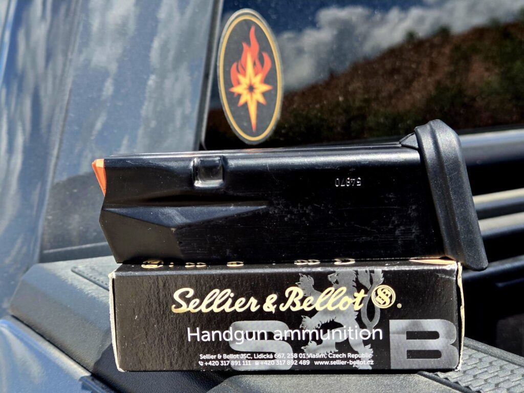 A pistol magazine on top of a single box of ammunition on the back of a pickup truck